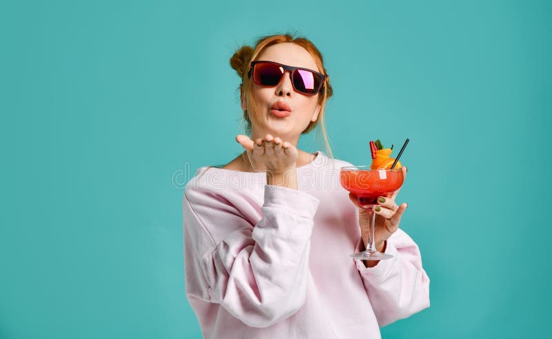 Clubbing young modern woman in fashion sunglasses holds a tropic cocktail strawberry margarita with a orange slice sends a kiss