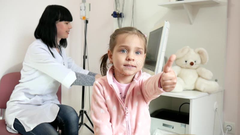 Clínica médica, sinal de sorriso da aprovação, retrato das mostras da criança da criança feliz na recepção do ` s do doutor, sent