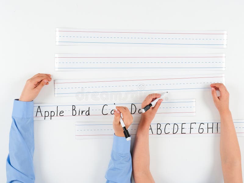 Clôture des élèves de l'école primaireEcriture manuelle sur papier. Une vue rapprochée des élèves de l'école primaire écrivant sur du papier doublé avec des phrases comme Apple Bird et ABCDEFGHI mis contre une carte magnétique vierge idéal pour les maquettes éducatives. Parfait pour présenter l'écriture dans un cadre de classe