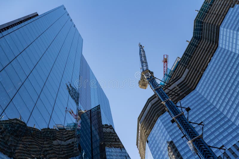 Clădire modernă în construcție, într-o zi însorită, pe fundalul albastru al cerului. reflexia macaralelor turnului pe oglinda fere stock images