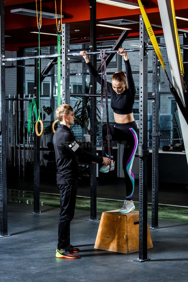 Intense workout in dark gym: Coach teaches to pull up on a horizontal bar beautiful girl. Intense workout in dark gym: Coach teaches to pull up on a horizontal bar beautiful girl