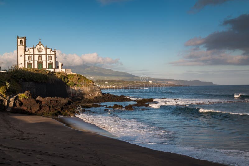 Coast of Sao Miguel Island, city Sao Roque. Church on a hill. Beach in the foreground. Cloudy sky. Azores Islands, Portugal. Coast of Sao Miguel Island, city Sao Roque. Church on a hill. Beach in the foreground. Cloudy sky. Azores Islands, Portugal.