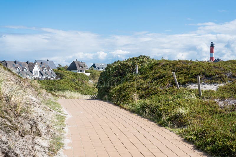 Cobbled footpath through dunes on the island of Sylt, Germany, with typical red and white lighthouse and buildings in background