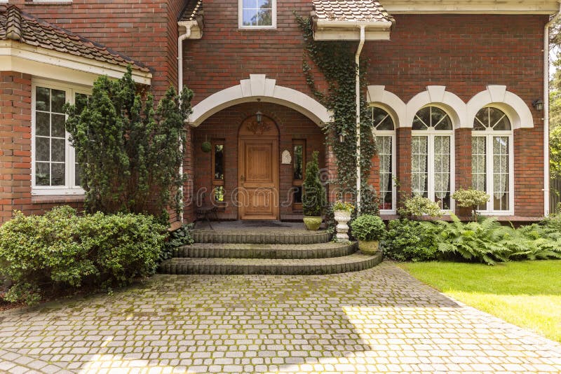 Cobbled path and steps leading to a stylish entryway with ornamented wooden door and side windows in a red brick English style ma