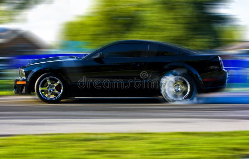 2009 Ford Mustang race car burnout. Black coupe with side stripe, cowl hood and chrome racing wheels shown with motion blur. 2009 Ford Mustang race car burnout. Black coupe with side stripe, cowl hood and chrome racing wheels shown with motion blur.