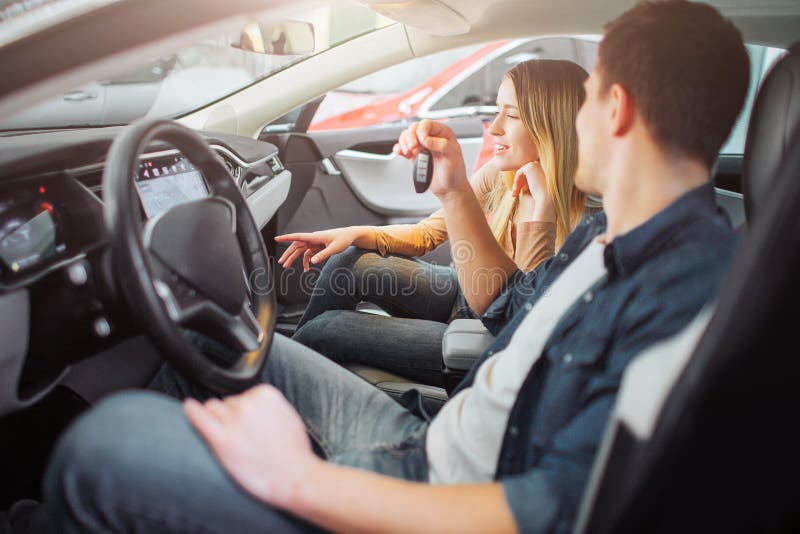 Coche eléctrico de compra de la familia joven primer en la sala de exposición Hombre atractivo detrás de la llave del coche de la foto de archivo Coche eléctrico de compra de la familia joven primer en la sala de exposición Hombre atractivo detrás de la llave del coche de la foto de archivo