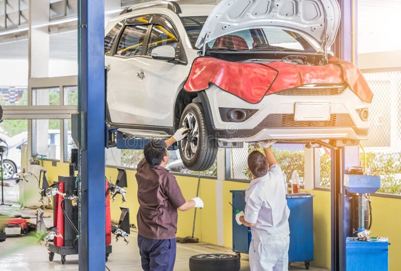 Coche en la elevación para reparar la suspensión en el garaje con el mecánico que trabaja por debajo el coche levantado al eje de imagenes de archivo Coche en la elevación para reparar la suspensión en el garaje con el mecánico que trabaja por debajo el coche levantado al eje de imagenes de archivo