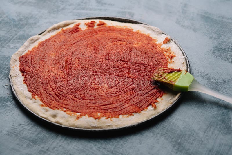 Cocinar la pizza italiana con los tomates, pollo, aceitunas en fondo de madera Salsa de tomate en la pasta por la mano de la muje imagen de archivo Cocinar la pizza italiana con los tomates, pollo, aceitunas en fondo de madera Salsa de tomate en la pasta por la mano de la muje imagen de archivo