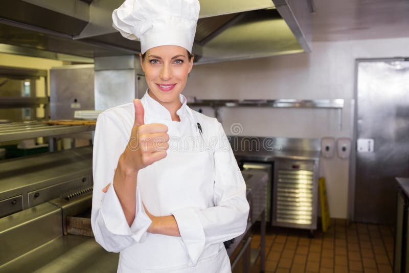 Cocinero de sexo femenino sonriente que gesticula los pulgares para arriba en cocina imagen de archivo libre de regalías Cocinero de sexo femenino sonriente que gesticula los pulgares para arriba en cocina imagen de archivo libre de regalías