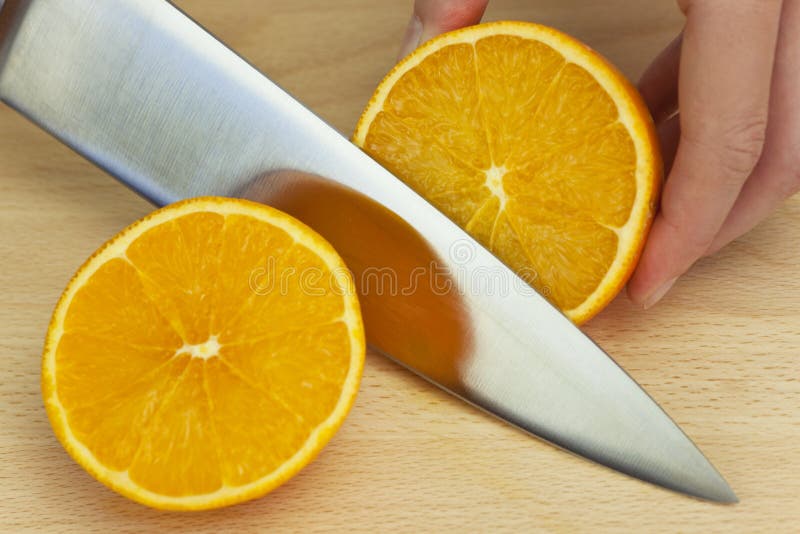 Cocinero que rebana la naranja fresca con el cuchillo de cocina sostenido