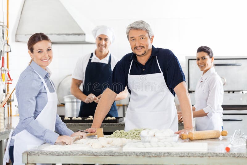 Cocineros de sexo masculino y de sexo femenino confiados que preparan las pastas en fotografía de archivo Cocineros de sexo masculino y de sexo femenino confiados que preparan las pastas en fotografía de archivo