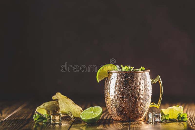 Cocktail alcoolique de mulet de Moscou dans la tasse de cuivre avec la monnaie royale et le citron écrasés de glace sur la table e
