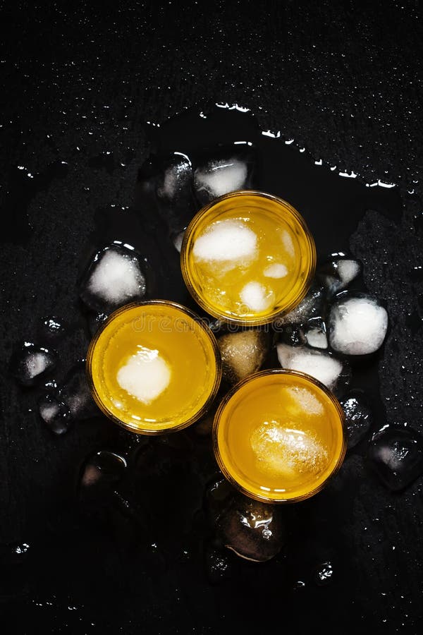 Cocktail amarelo com gelo no fundo escuro molhado, vista superior imagem de stock Cocktail amarelo com gelo no fundo escuro molhado, vista superior imagem de stock