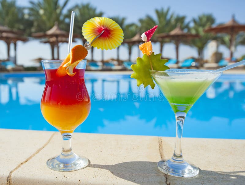 Two cocktail drinks by a tropical resort swimming pool. Two cocktail drinks by a tropical resort swimming pool