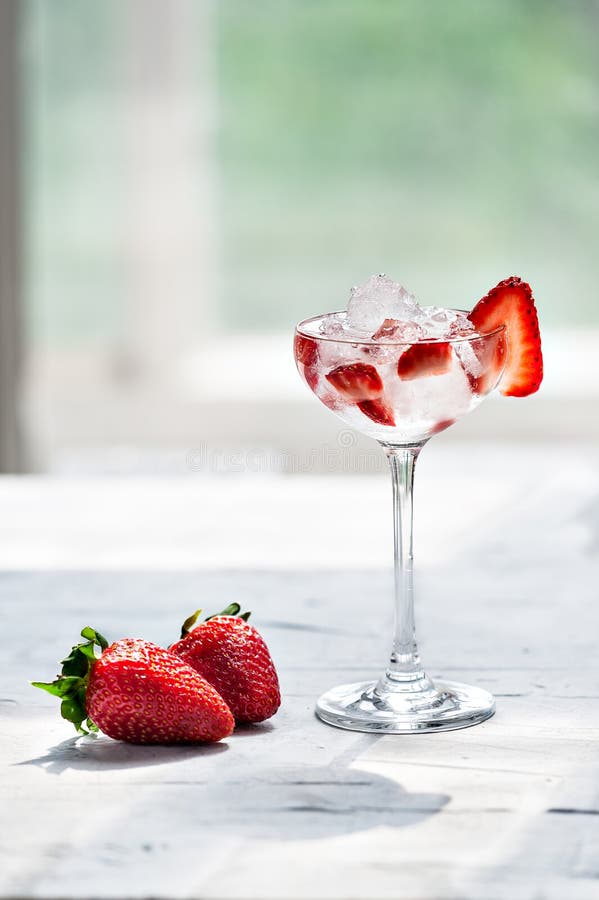 Cocktail freddo con vodka, lo sciroppo di fragole, le fragole fresche ed il ghiaccio tritato in vetri su un fondo leggero fotografia stock libera da diritti Cocktail freddo con vodka, lo sciroppo di fragole, le fragole fresche ed il ghiaccio tritato in vetri su un fondo leggero fotografia stock libera da diritti