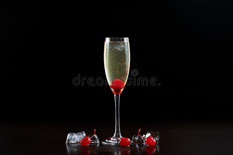 Cocktail glass with cold champagne, ripe red cherries and ice cubes isolated on black background.