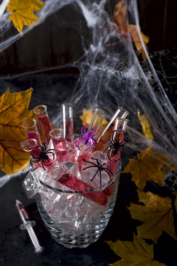 Cocktail in glass tubes in an ice bucket for Halloween party celebration with black spiders and a spider web in the background, copy space. Cocktail in glass tubes in an ice bucket for Halloween party celebration with black spiders and a spider web in the background, copy space