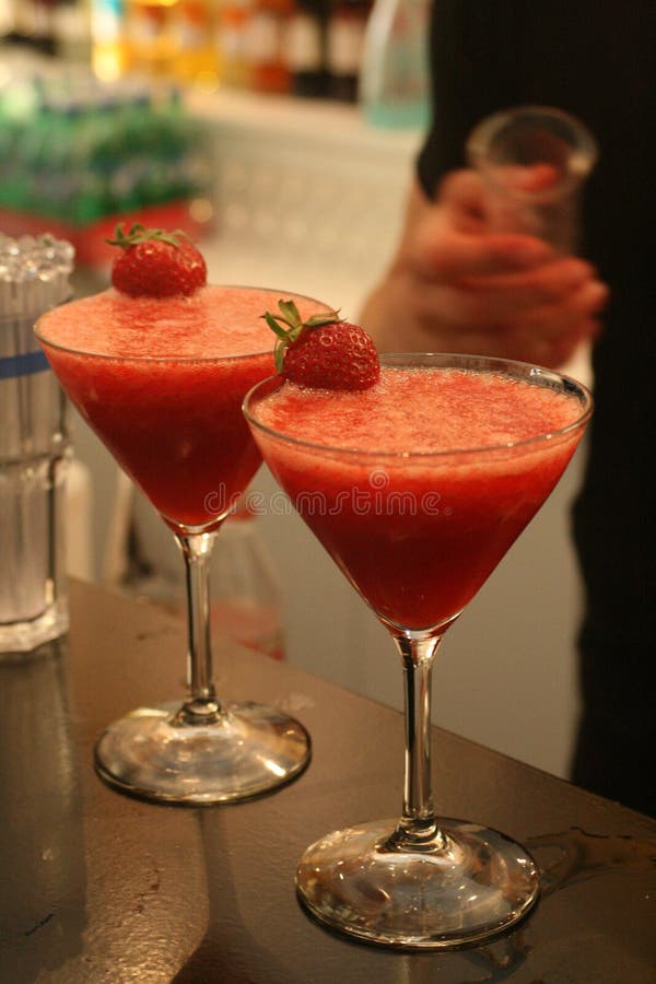 Due bicchieri pieni di deliziosi rosso Strawberry Daiquiri cocktail in piedi sul bancone di un bar davanti a un barman.