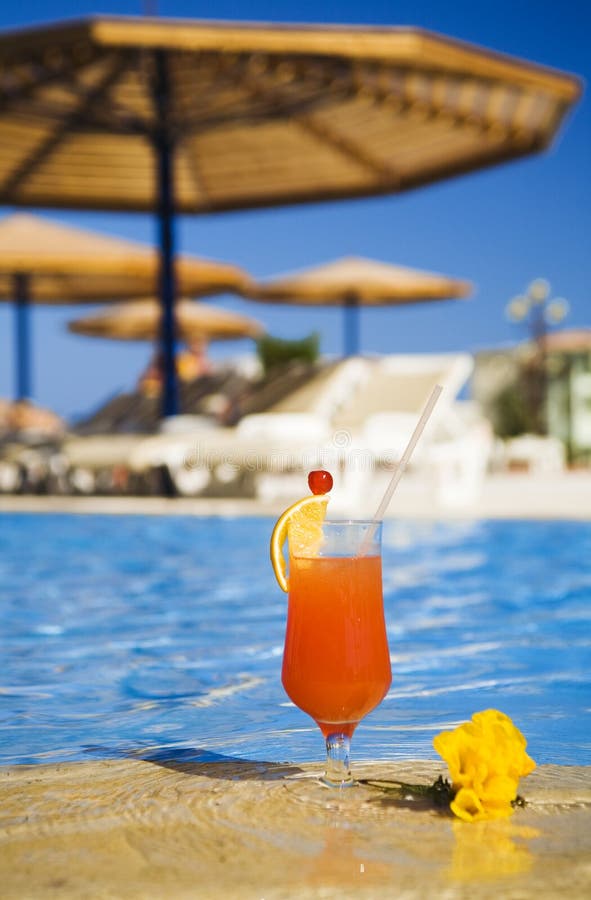 Orange cocktail stands on edge of swimming-pool near a flower. Traditional resting. Orange cocktail stands on edge of swimming-pool near a flower. Traditional resting.