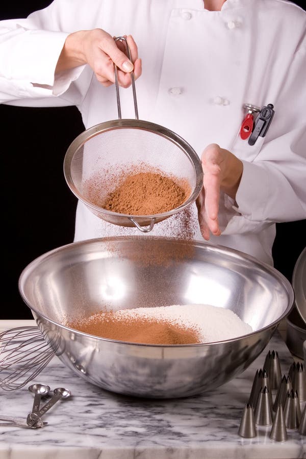 Chiudere l'azione di acquisizione di una uniforme Pasticcere mentre setacciando il cacao in polvere in acciaio inox, con ampia terrina contenente setacciato la farina dolce.