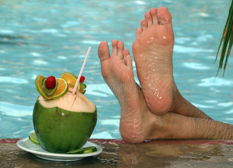 Coconut cocktail on the edge of the pool with male feet crossed beside