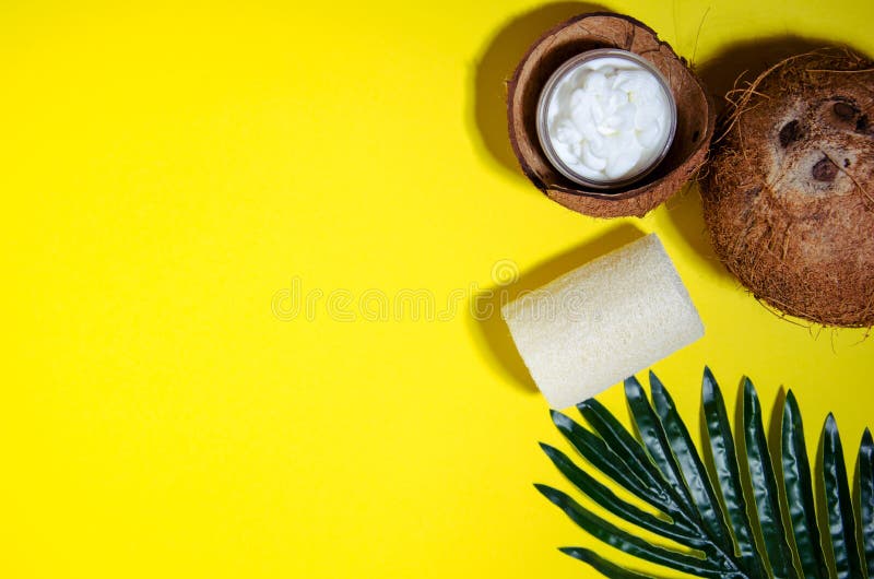 Cosmetic attributes: a cream in a jar lies in a half of a coconut, a loofah washcloth lie on a yellow background. Near coconut and palm leaf. Flat lay, hard shadows. Horizontal view. Cosmetic attributes: a cream in a jar lies in a half of a coconut, a loofah washcloth lie on a yellow background. Near coconut and palm leaf. Flat lay, hard shadows. Horizontal view