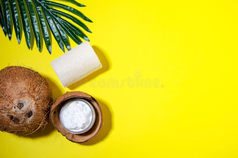 Cosmetic attributes: a cream in a jar lies in a half of a coconut, a loofah washcloth lie on a yellow background. Near coconut and palm leaf. Flat lay, hard shadows. Horizontal view. Cosmetic attributes: a cream in a jar lies in a half of a coconut, a loofah washcloth lie on a yellow background. Near coconut and palm leaf. Flat lay, hard shadows. Horizontal view