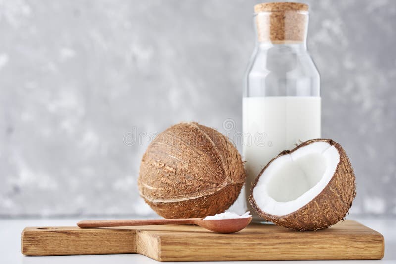 Coconut Milk in Glass Bottle and Fresh Coconuts with Half on a Gray