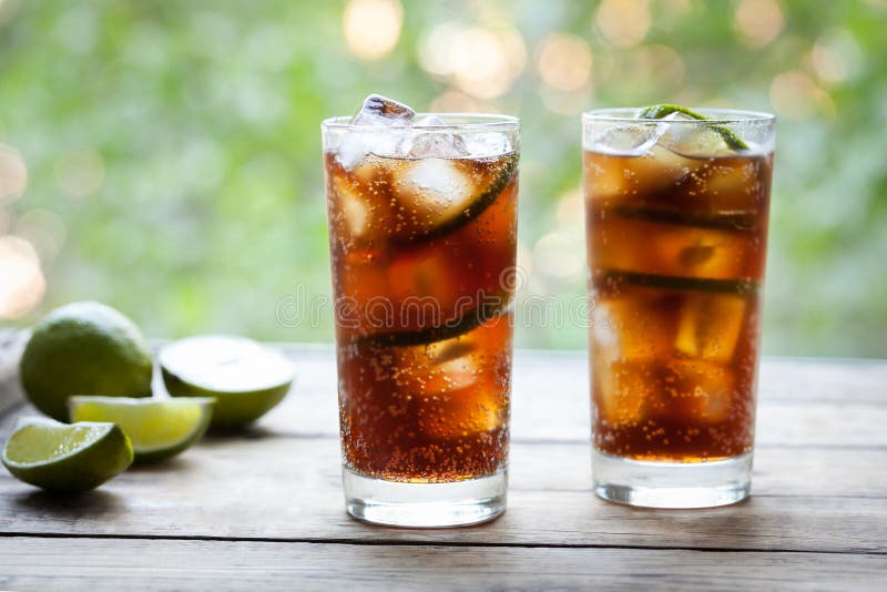 Coctail för KubaLibre uppfriskande sommar med en cola, en is, en limefrukt och en rom på trätabellen med en sikt till terrassen o royaltyfri bild