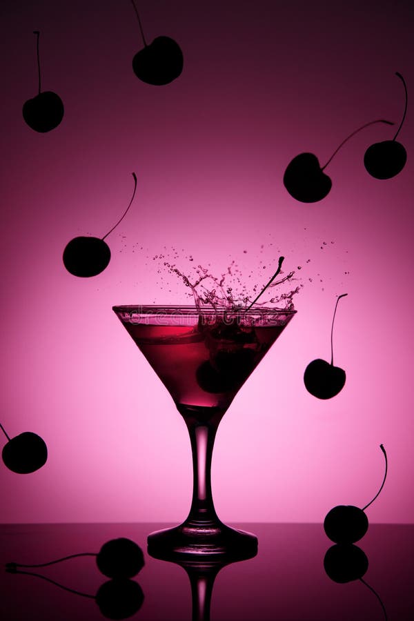 Coctail rosado de la cereza en el vidrio de martini con un chapoteo y las cerezas que caen en el fondo imagen de archivo libre de regalías Coctail rosado de la cereza en el vidrio de martini con un chapoteo y las cerezas que caen en el fondo imagen de archivo libre de regalías