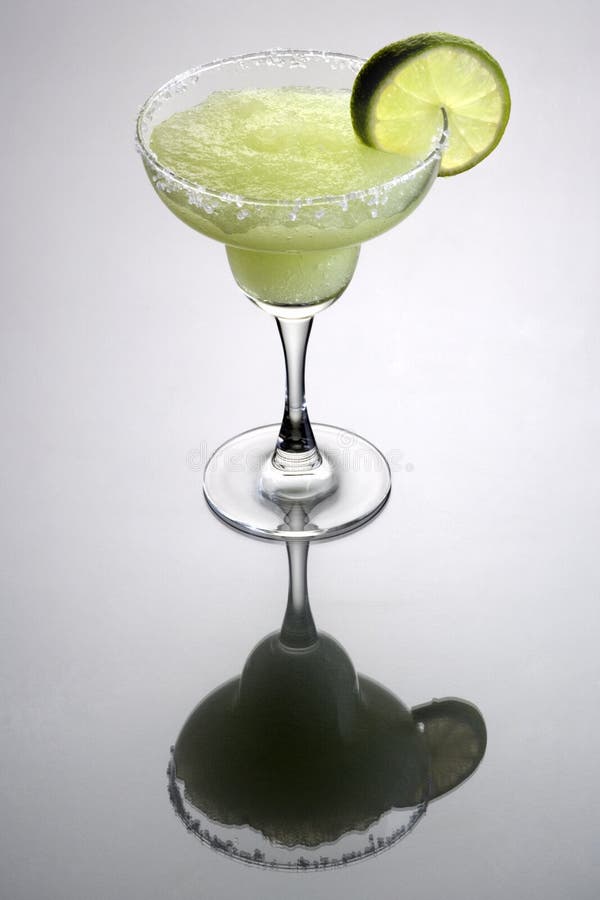 Frozen Margarita mixed drink with lime slice garnish on plain grey background with reflection. Frozen Margarita mixed drink with lime slice garnish on plain grey background with reflection