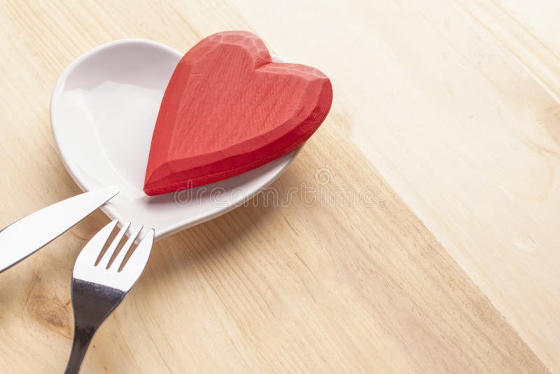 Coeur rouge d'un plat blanc sous forme de coeur sur un fond en bois avec une fourchette et un couteau image stock Coeur rouge d'un plat blanc sous forme de coeur sur un fond en bois avec une fourchette et un couteau image stock