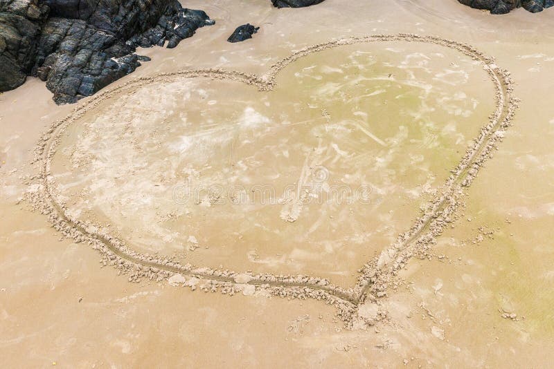 Coeur sur une plage de sable avec la roche comme fond photos stock Coeur sur une plage de sable avec la roche comme fond photos stock