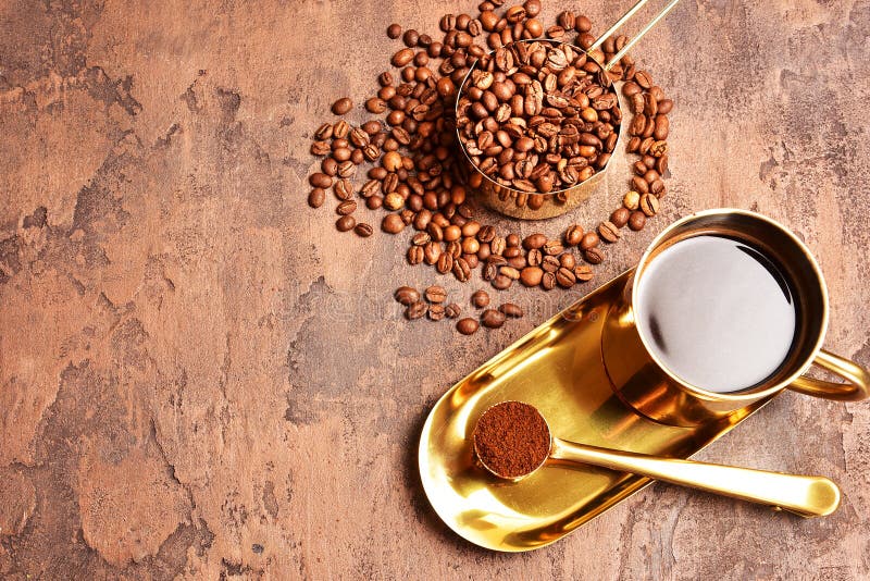 Coffee Beans, Golden Cup of Coffee on a Brown Background. Stock Image