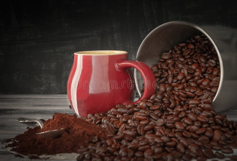 Coffee beans spilled out of a tin can onto a wooden table. Near the burgundy cup and freshly ground coffee. Photo in dark style royalty free stock image Coffee beans spilled out of a tin can onto a wooden table. Near the burgundy cup and freshly ground coffee. Photo in dark style royalty free stock image