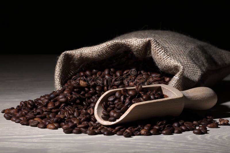 Coffee beans on a wood surface with a scoop and hessian sack