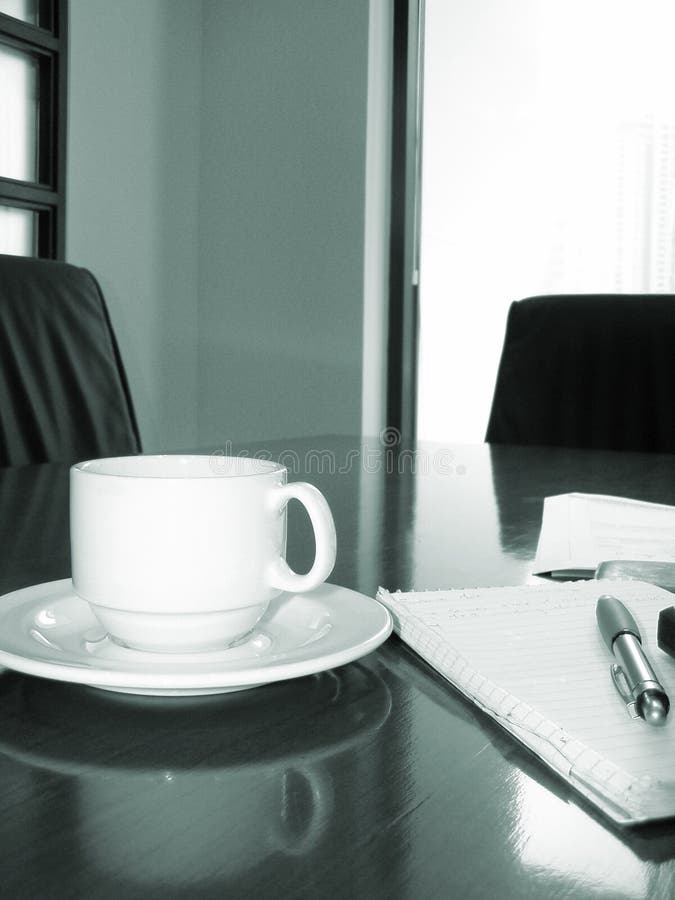 Colpo di una riunione o un tavolo per la sala riunioni in ufficio con un blocco per appunti, penna e tazza di caffè.