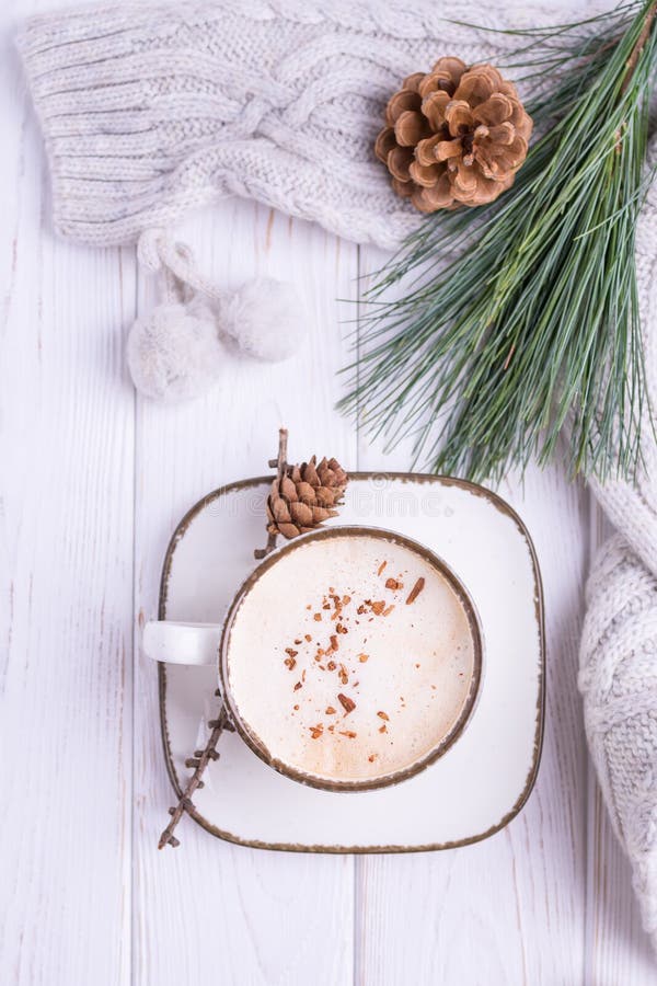 Coffee cappuccino with ceylon cinnamon, a branch of a pine tree and knitted accessories on a white wooden background