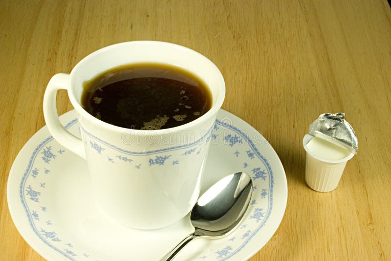 A coffee cup full of coffee with saucer spoon and cream. A coffee cup full of coffee with saucer spoon and cream