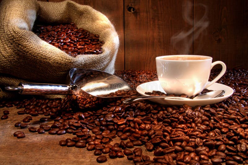 Tazza di caffè con un sacco di tela ruvida di chicchi di caffè tostati sul tavolino.