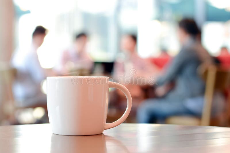 Šálek kávy na stole s lidmi v kavárně jako je rozmazání pozadí.