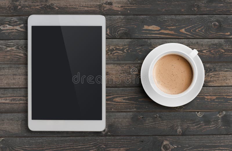 Coffee cup and tablet pc similar to ipad on dark wooden table top view