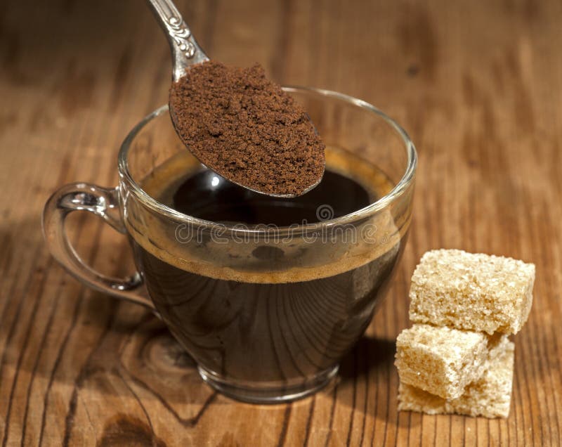 Glass coffee cup and spoon with instant granulated coffee on old wooden background.