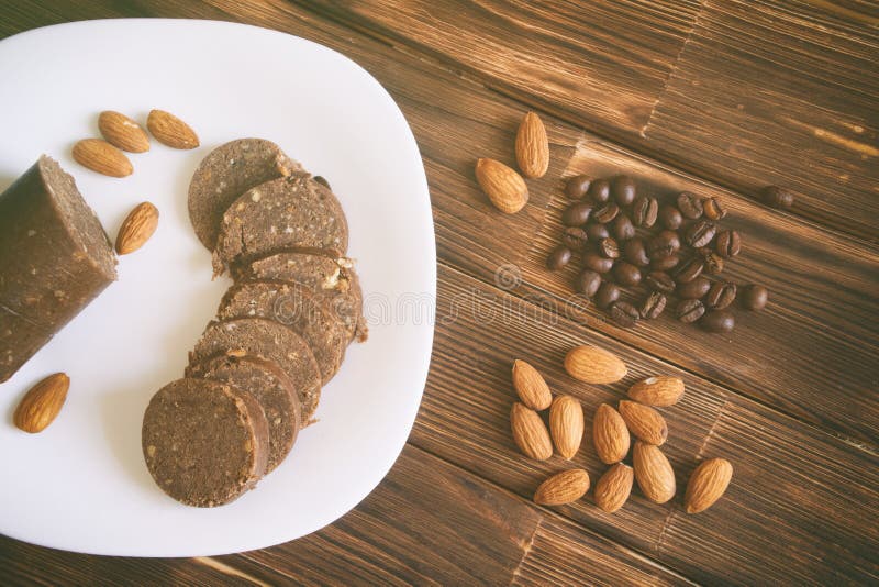 Coffee grains, almond nuts and chocolate pastry sausage on a wooden surface. Rustic still life