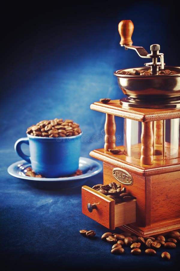 Coffee grinder with beans and cup on saucer standing on blue tab