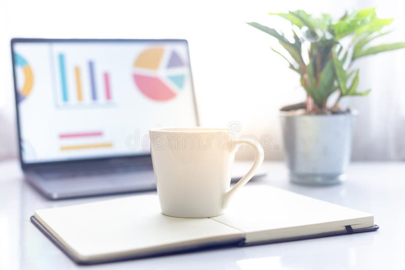 Coffee on Notebook with Laptop on White Table in the Morning Sun Light