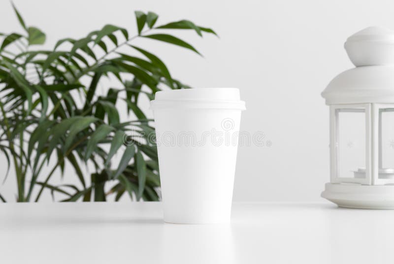 Coffee paper cup mockup with a candle holder and a palm plant on a white table