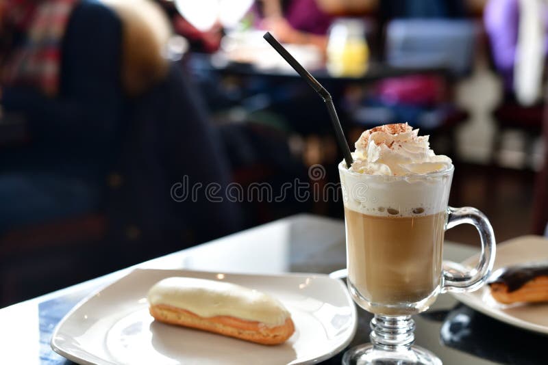 Coffee with Whipped Cream and Eclair on Table in a Cafe Stock Image