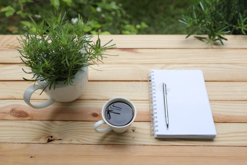 Coffee with White Notebook and Green Plant on Wooden Table at Exterior