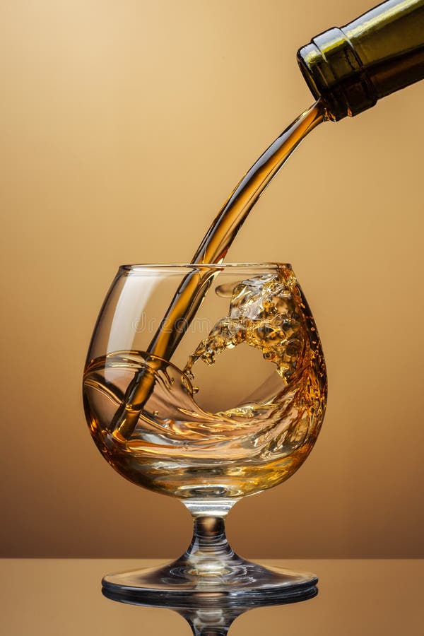 Cognac pouring from bottle into glass with splash on brown